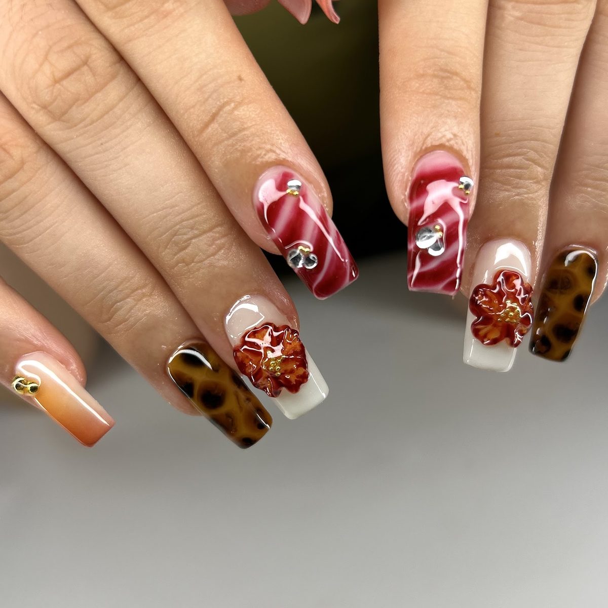 Ongles longs en marbre rouge, écaille et fleurs sculptées en relief au cœur de perles d’or
